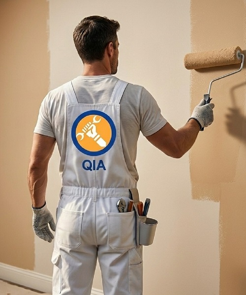 QIA painter applying interior wall paint with roller — house painting services Dammam
